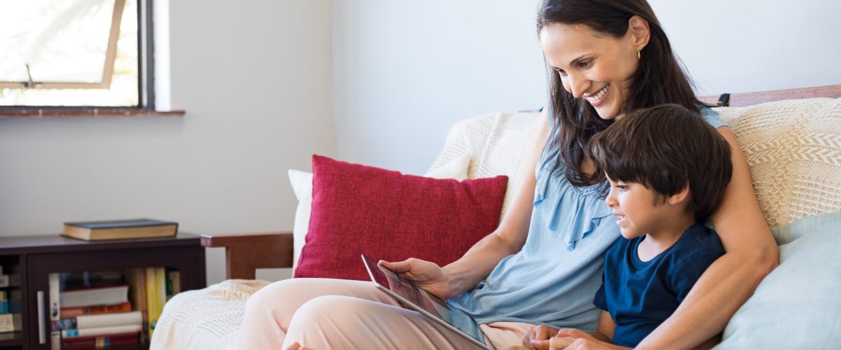 Mother and son sitting on a couch using tablet together